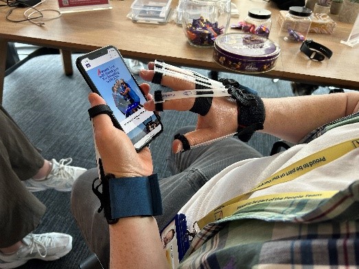 A photo of someone's hands holding a phone. The person is wearing a device on their hands to reduce their ability to move their fingers to simulate having reduced motor function. 